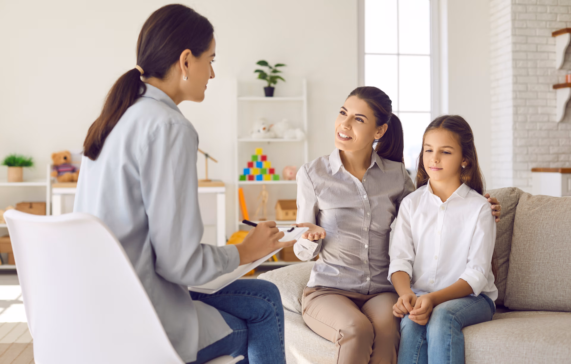 happy young mother and her little daughter talk to female psychotherapist during therapy session.